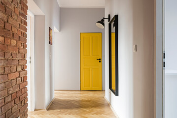 Przedpokój z ceglaną ścianą i dużym lustrem oraz żółtymi drzwiami - obrazy, fototapety, plakaty