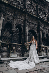 Fototapeta premium Charming bride in a long white wedding dress on a background of black old building