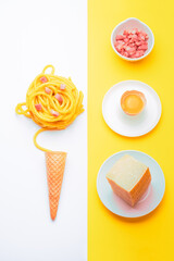 carbonara pasta with ingredients next to it on a bright yellow and white symmetrical background rolled in the shape of a ball above an ice cream cone shot in plan and vertical