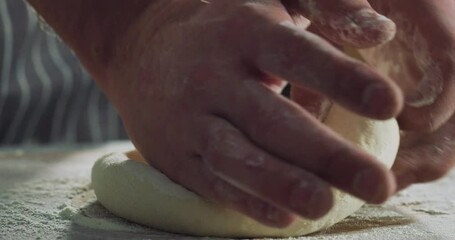 Cinematic macro shot of professional artisan baker chef kneading just prepared loaf of dough for better levitation for preparation of pasta, pizza and other pastries in rustic bakery kitchen.