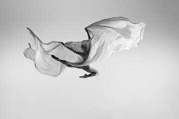 Black and white portrait of graceful ballerina dancing with fabric, cloth isolated on grey studio...