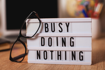 Busy doing Nothing. light box sign sitting on top of a desk. glasses and a desktop. in the...