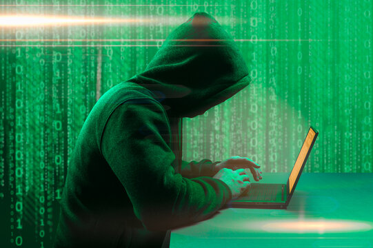 Hacker attack. Faceless hooded anonymous computer hacker. hooded hacker sitting near computer monitors. dark green background. side view. dark web