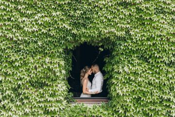 Bride in white wedding dress and groom in the window, from the building fully covered with leaves