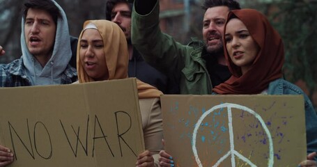 Group of young confident activists pacifists with placards with symbol of peace and phrase "no war" protesting against war and violence during manifestation.