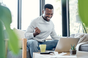 Debt free is the life for me. Shot of a young man celebrating while going over paperwork and using a laptop at home.