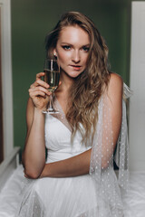 Brides morning. Bride drinking champagne in the peignoir. young woman is sitting on bed in a hotel room. wedding day.