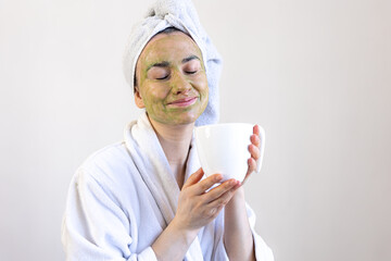 Young woman with a green beauty mask on her face and with a cup.