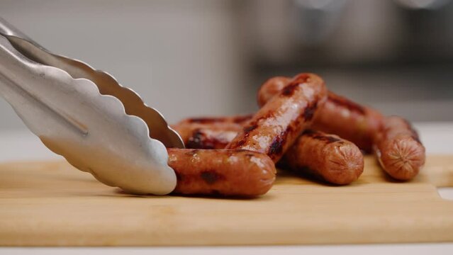 Setting a sausage link down on cutting board with tongs for breakfast in bright kitchen in slow motion 4k