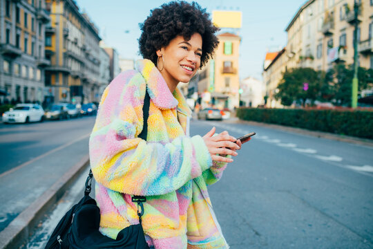 Young black smiling curly hair woman outdoor walking using smartphone - Powered by Adobe