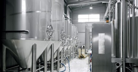 Panning shot of rows of large steel tanks with beer in industrial brewery plant. Stainless steel tanks for brewing beer. automatized process. Modern Beer Factory. Brewery concept. Brewing equipment - Powered by Adobe