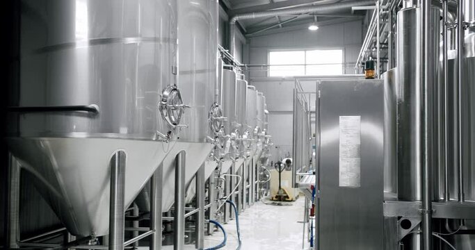 Panning shot of rows of large steel tanks with beer in industrial brewery plant. Stainless steel tanks for brewing beer. automatized process. Modern Beer Factory. Brewery concept. Brewing equipment