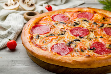 Pepperoni pizza with mushrooms and vegetables on grey wooden table macro close up
