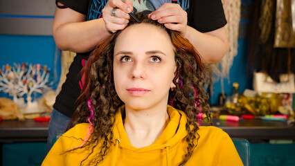 Unrecognizable person makes hairstyle for young woman in salon. Professional hairstylist makes hairdo for client.