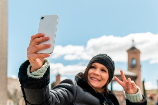 Woman With A Black Hat Grabbing Her Cell Phone To Take A Selfie In The Historic Center Of The City. Middle Aged Girl Making A Video Call With Her Friend Or Her Partner With The City Background.