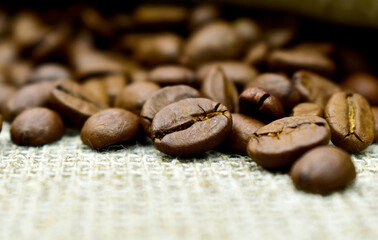Coffee beans scattered on burlap, close-up, blurred background