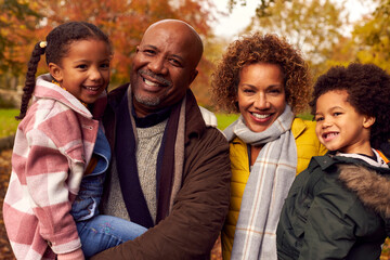 Portrait Of Grandparents Carrying Grandchildren On Walk Through Autumn Countryside Together