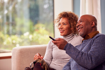 Senior Couple Sitting On Sofa At Home Watching TV Together