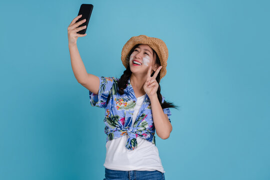 Beautiful young asian woman wear colorful shirt for sonkran festival use smart mobile phone on blue background. She is taking pictures of yourself
