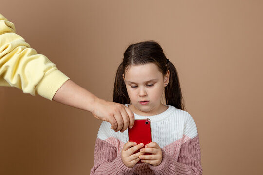 Portrait Of Parent Taking Smartphone Away From Girls Hands, Beige Background. Little Daughter Hold Tight Phone And Resist. Concept Of Prevention Of Telephone Addiction In Children, Nomophobia.