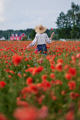 Summertime. Young woman in hat walking on red poppy field.