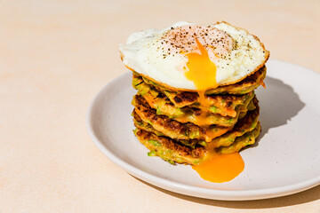 Close-up of a stack of fried vegetable pancakes, made from zucchini and carrot, with a fried egg...