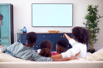 Rear View Of Family Sitting On Sofa Watching Movie On TV At Home