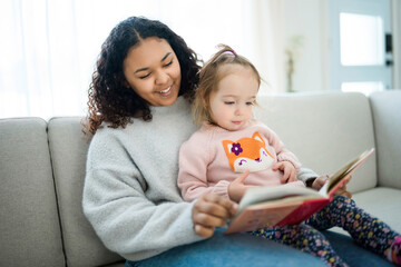 babysitter black woman read book with little child girl - obrazy, fototapety, plakaty