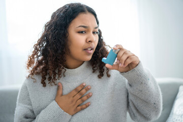 black woman taking her inhaler at home at the living room