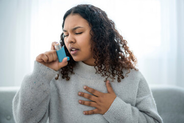black woman taking her inhaler at home at the living room - Powered by Adobe