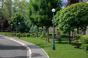 an asphalt road with a stone curb and a tarmac pedestrian sidewalk near a park with trees and...