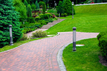 iron ground lantern and poli garden lighting of park curved path paved with stone tiles with drain...