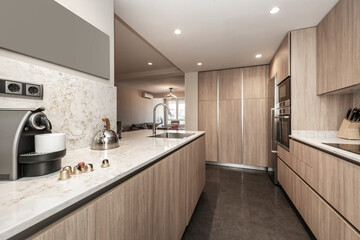 Kitchen with oak furniture, integrated appliances, white stone countertop and dark stoneware floor and access to a glazed terrace with coffee maker, ceramic hob and stainless steel sink.