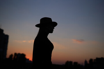 Silhouette of happy fashionable long hair woman wearing hat at sunset. Image against sun and blue sky. High quality photo