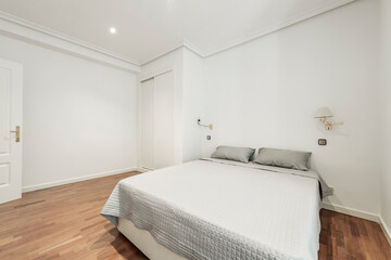Fototapeta na wymiar Bedroom with a double bed with a gray bedspread, a built-in wardrobe with white sliding doors and a reddish oak parquet floor in a vacation rental apartment