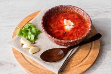 Freshly brewed delicious borscht soup on a linen napkin with garlic and parsley in a clay bowl.