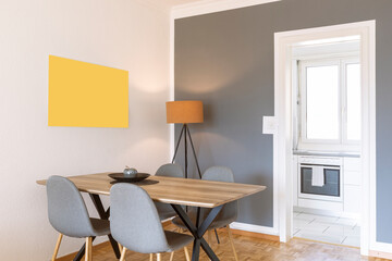 Detail of modern table and chairs with parquet floor, yellow frame and grey wall. Open door to the kitchen . Nobody inside