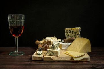 Still life with Manchego cured sheep cheese and French blue cheeses with knives and garlic and a glass of Spanish rose wine