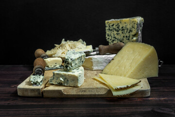 Still life with cured sheep's Manchego cheese, Italian Parmesan cheese flakes and French blue cheeses with knives and garlic on a wooden board