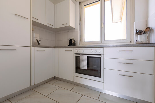 Small modern white kitchen with oven, coffee maker and stove with large bright window with a view.