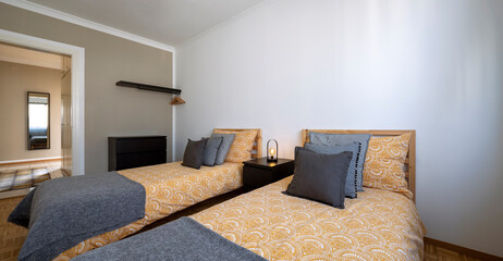 Bedroom with two single beds, white walls and gray and yellow blankets. Pillows above the beds....
