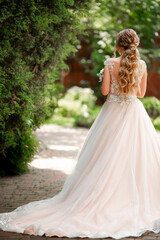 A beautiful bride holds a bouquet of roses in her hands and waits for her groom. Wedding traditions. Good weather in summer, when all around are bright and green leaves
