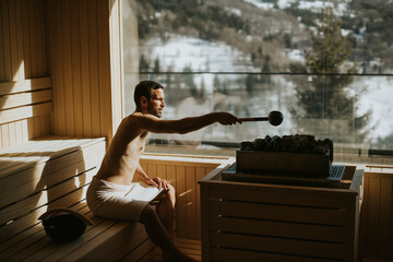 Young man pouring water onto hot stone in the sauna