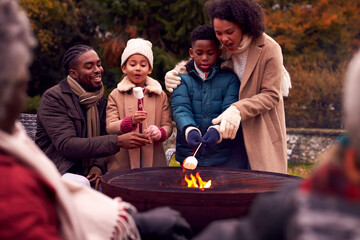 Multi-Generation Family Having Fun Toasting Marshmallows In Autumn Garden Together