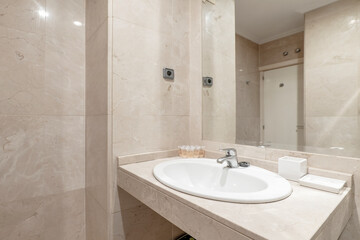 bathroom with white porcelain sink on marble countertop, cream marble walls and wall mounted frameless mirror in vacation rental apartment