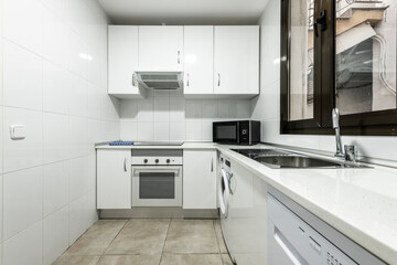 L-shaped kitchen with white cabinets and white stone countertops, matching appliances and black countertop microwave oven