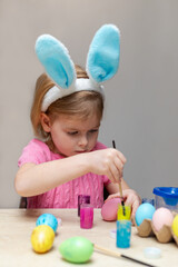 Little girl in Easter bunny ears painting Easter eggs. Holiday crafts for children