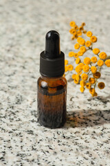 Bottle with dropper pipette with serum or essential oil. Grey granite background with daylight and yellow flowers. Skincare products, natural cosmetic. Beauty concept for face and body care