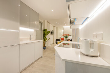 Open kitchen with white cabinets and built-in appliances, white stone countertops and small appliances above it
