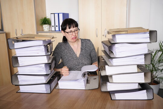 Sekretärin mit übervollem Schreibtisch mit Aktenbergen, ist nagativ und unmotiviert zu ihrer Arbeit eingestellt